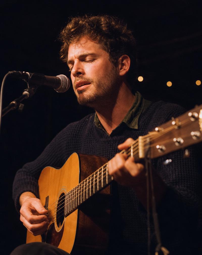 Folk musician performing with an acoustic guitar at a small venue